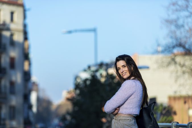 Woman in casual wear standing outside with arms crossed on a sunny day