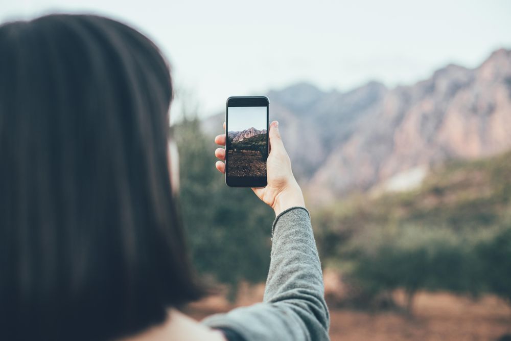 Woman with dark hair taking picture of mountain with smart phone