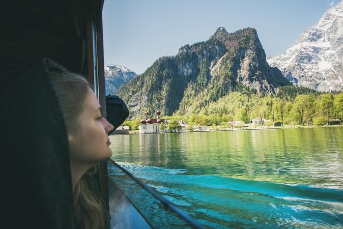 Young woman traveler looking out of window over mountains and water on boat trip