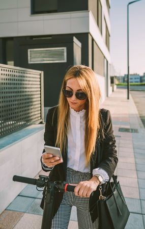 Businesswoman with e-scooter looking at cellphone