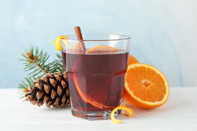 Glass of tasty mulled wine with orange on blue wooden background, space for text