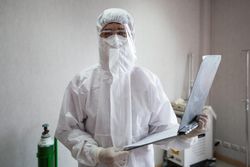 Portrait of doctor in PPE suit holding patient clipboard at emergency room in hospital