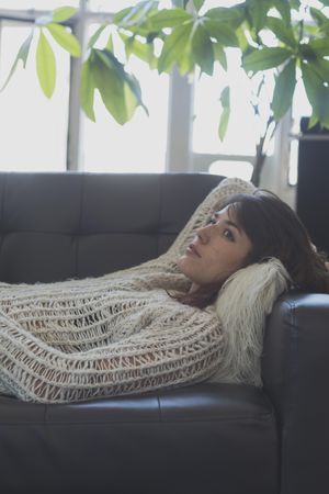 Female in wooly sweater lying on leather couch in living room, vertical