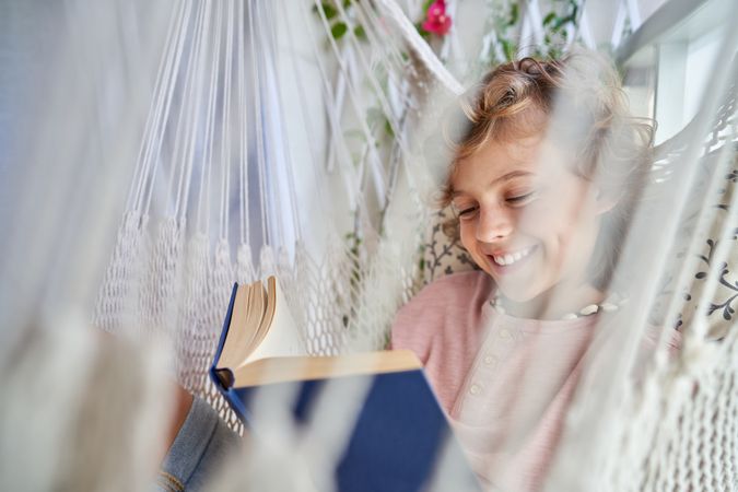 Cheerful kid with book in hammock