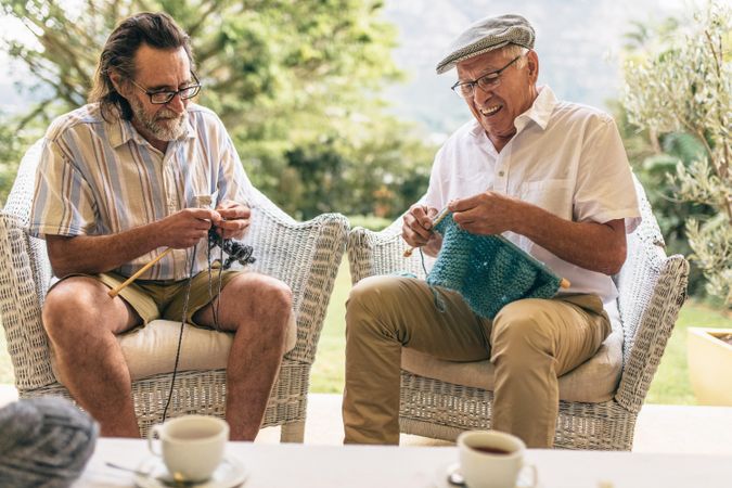 Two men sitting on armchair and knitting