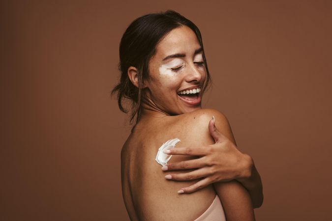 Side view of a woman with vitiligo and applying cream to her back