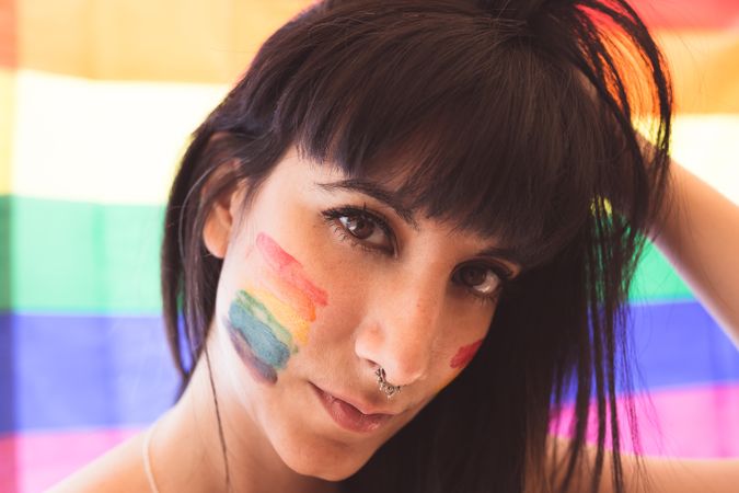 Brunette woman with LGBTQIA symbol on face straightening hair