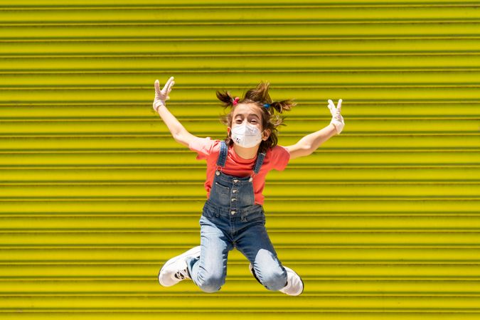 Cute child jumping in protective mask against a yellow wall