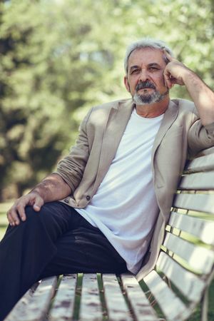 Portrait of a mature man, lost in thought on bench in a park