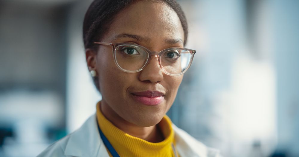 Portrait Close Up of Young Black Female Specialist Wearing Lab Coat and Glasses Smiling.