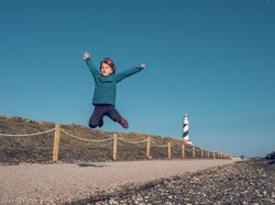 Boy jumping against lighthouse in countryside