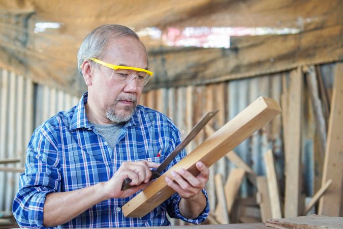 Asian male carpenter using ruler on wooden panel