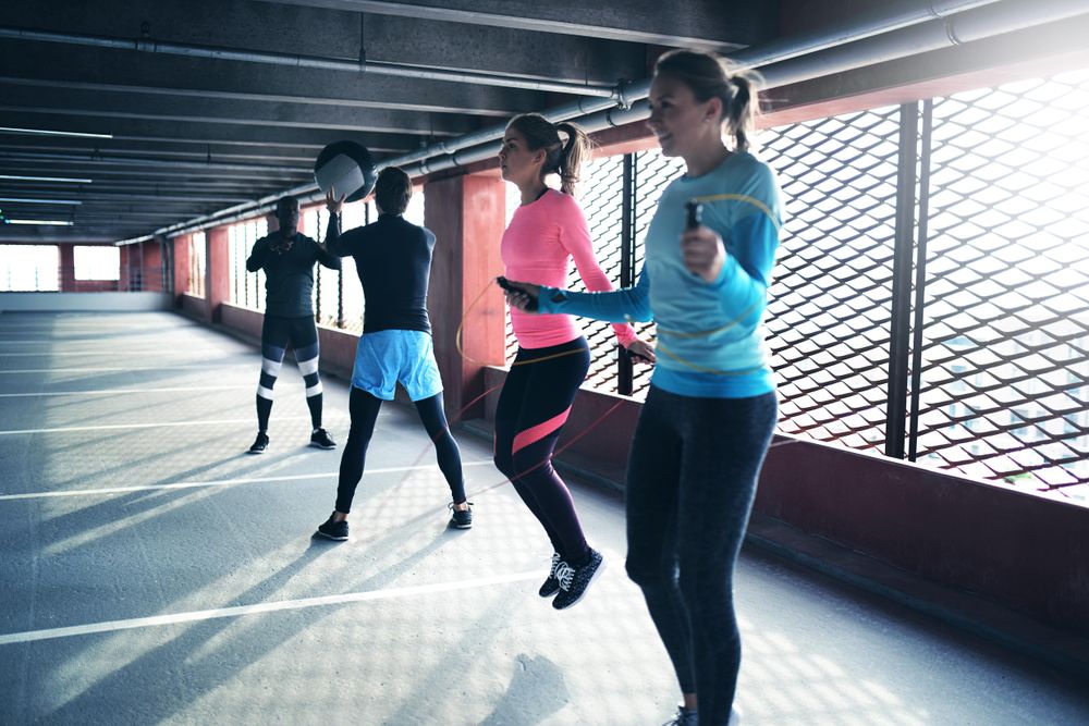 Two men throwing a medicine ball and two women jumping rope