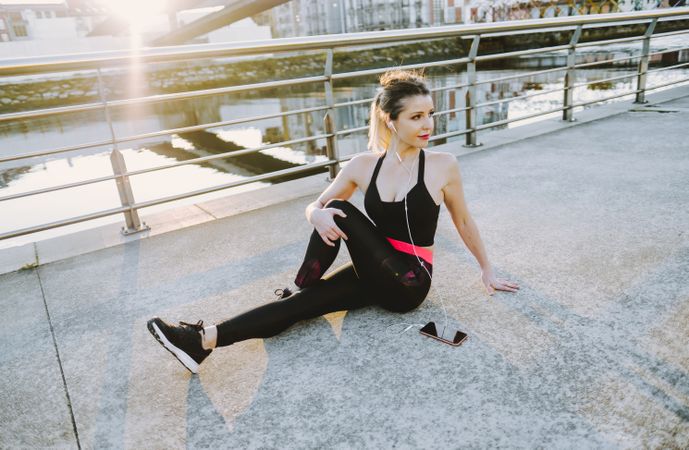 Woman with earphones and smartphone stretching on embankment