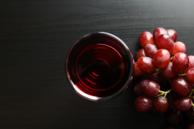 Grapes and glass with wine on dark table, top view