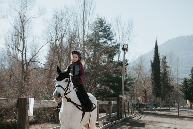 Little girl riding horse in enclosure