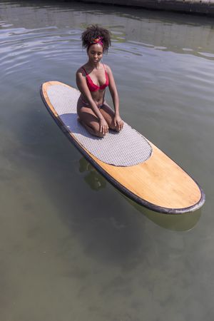 Black woman sitting on wooden paddle board in sea