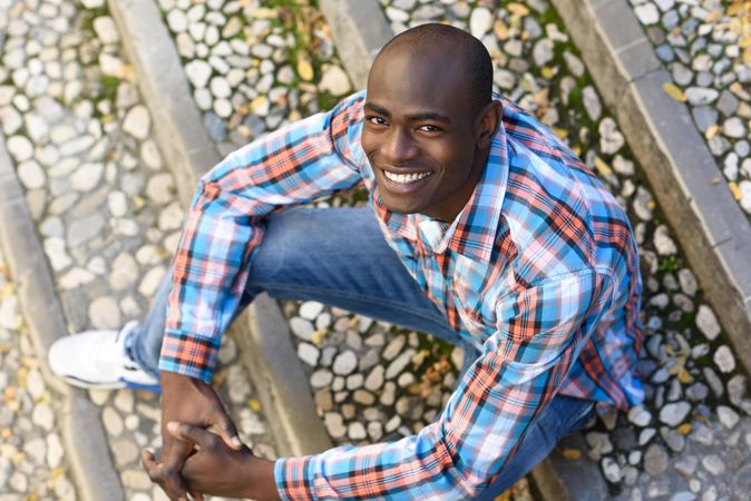 Happy male in plaid shirt sitting on stairs and looking up