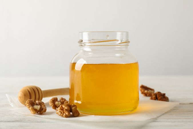 Walnuts, dipper, parchment and glass jar with honey on neutral background, copy space