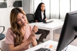 Asian woman holding her sore wrist while sitting at her desk