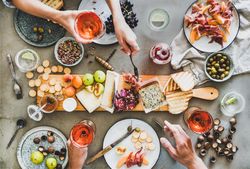 Charcuterie board with hands holding glasses of rose and serving prosciutto