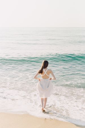 Back view of woman in light dress standing on beach