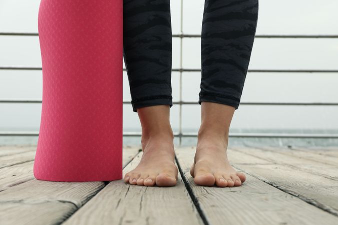 Female feet and pink yoga mat on wooden floor outdoors, close up