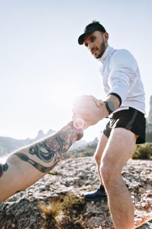 Athletic man helps friend onto rocks