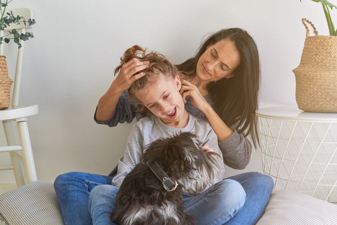Mother doing hairstyle to adorable son near dog