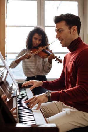 Man playing piano near woman playing violin in studio