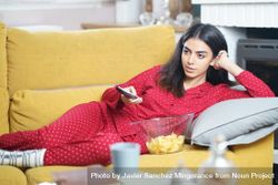 Woman in red pajamas relaxing on sofa with bowl of chips and remote control 5pdPg5