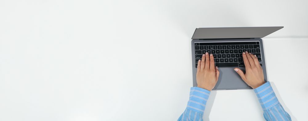 Top view of person using silver laptop on desk with copy space
