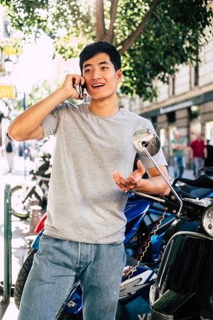 Confident Asian man talking on phone while standing by motorbike