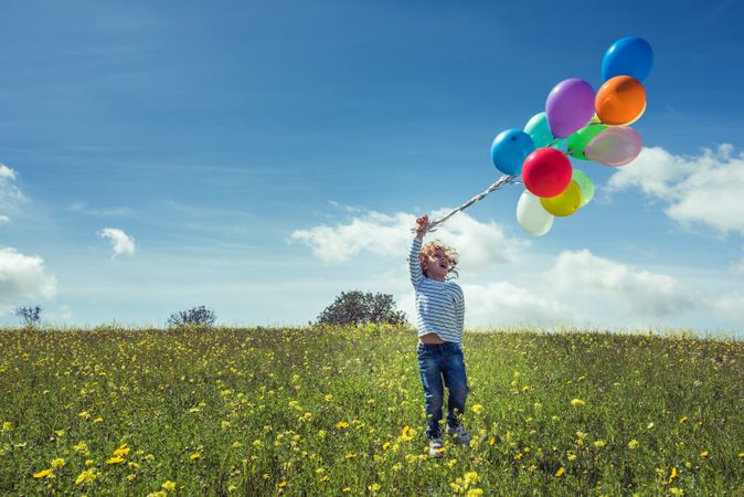 Excited kid holding balloons in grassy countryside