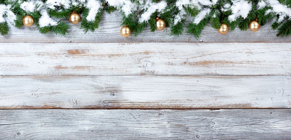 Snowy Christmas evergreen branches and golden ornaments on vintage wooden planks