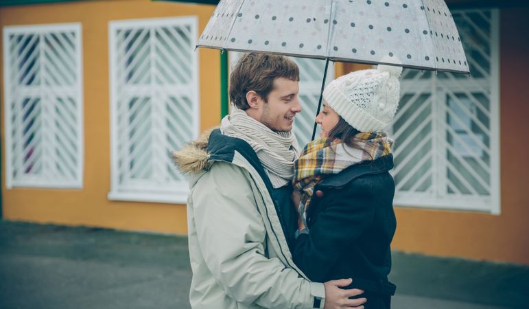 Portrait of cute couple embracing under the umbrella on an autumn rainy day