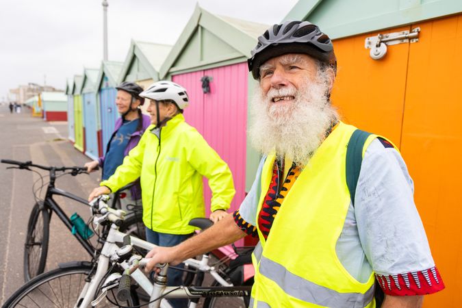 Three older people with bicycles standing in front of colorful sheds