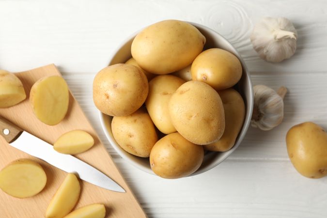 Top view of bowl full of potatoes on kitchen counter with garlic and knife