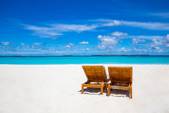Reclining chairs on a beach with blue sky with clouds