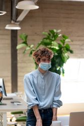 Nonbinary person standing in a bright modern office wearing a face mask