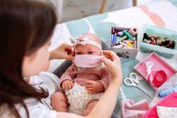 Girl trying on her doll a mask that she is sewing