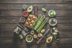 Various healthy cooking ingredients: green asparagus bunch, eggs, spices, avocado, lime,  olive oil and kitchen utensils
