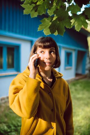 Smiling woman using smartphone near countryside house