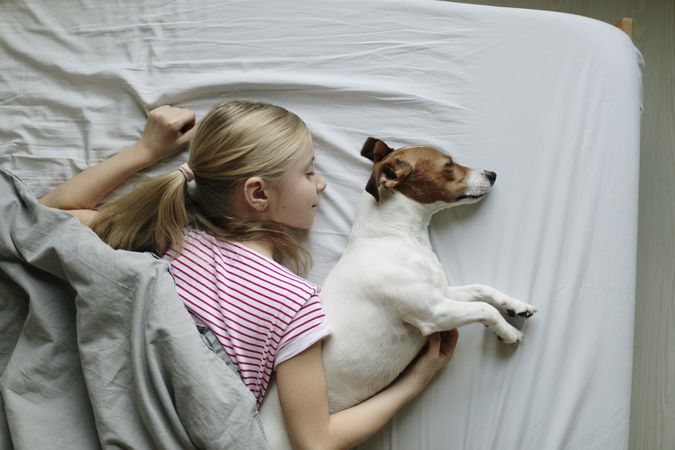 Top view of young girl smiling in her sleep with are around her dog