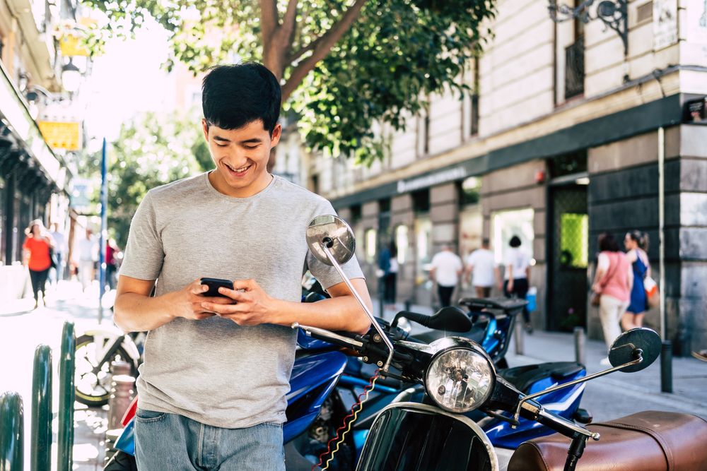 Confident Asian man talking on phone while standing by motorbike