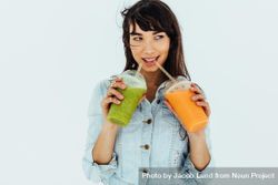 Portrait of beautiful woman drinking fresh orange and green juices on light background 5XPvG5