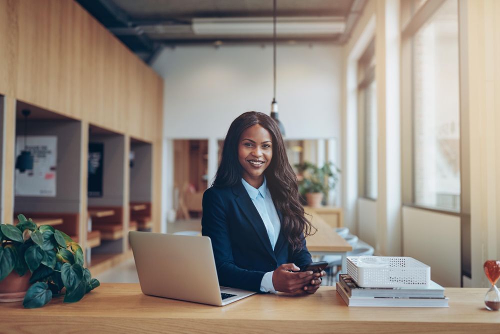 Woman standing at laptop smiling with smart phone