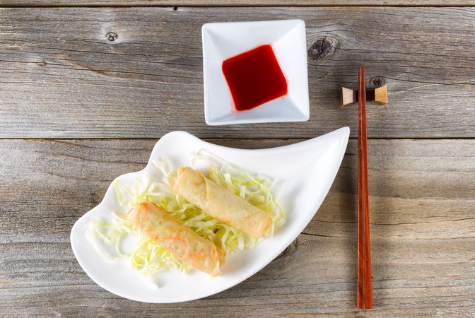 Fried Chinese spring rolls and sweet dipping sauce in bowl on rustic wood