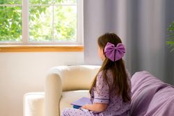 Girl wearing purple bow looking out window, contemplative.