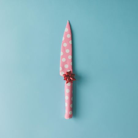 Knife wrapped in pink dotted paper with bow on blue background